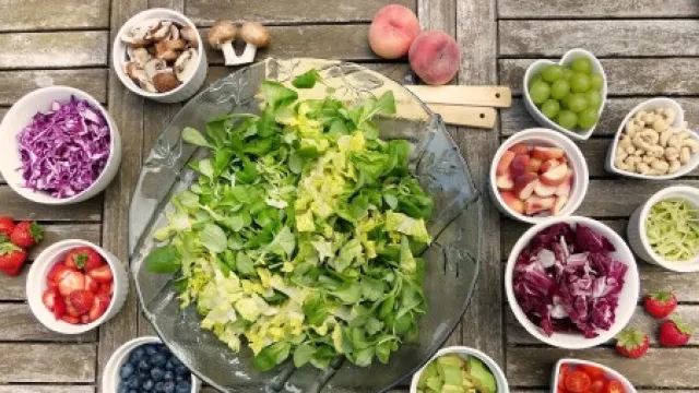 Verschieden Obst und Gemüsesorten in kleinen Schälchen um einen großen Teller mit grünem Salat